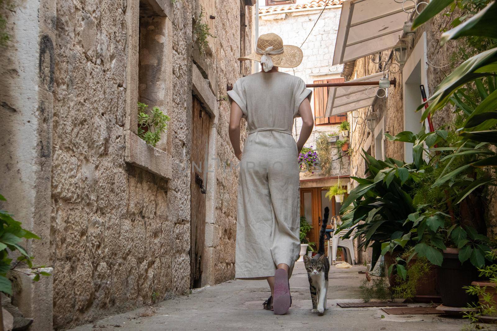 Rear view of beautiful blonde young female traveler wearing straw sun hat sightseeing and enjoying summer vacation in an old traditional costal town at Adriatic cost, Croatia by kasto