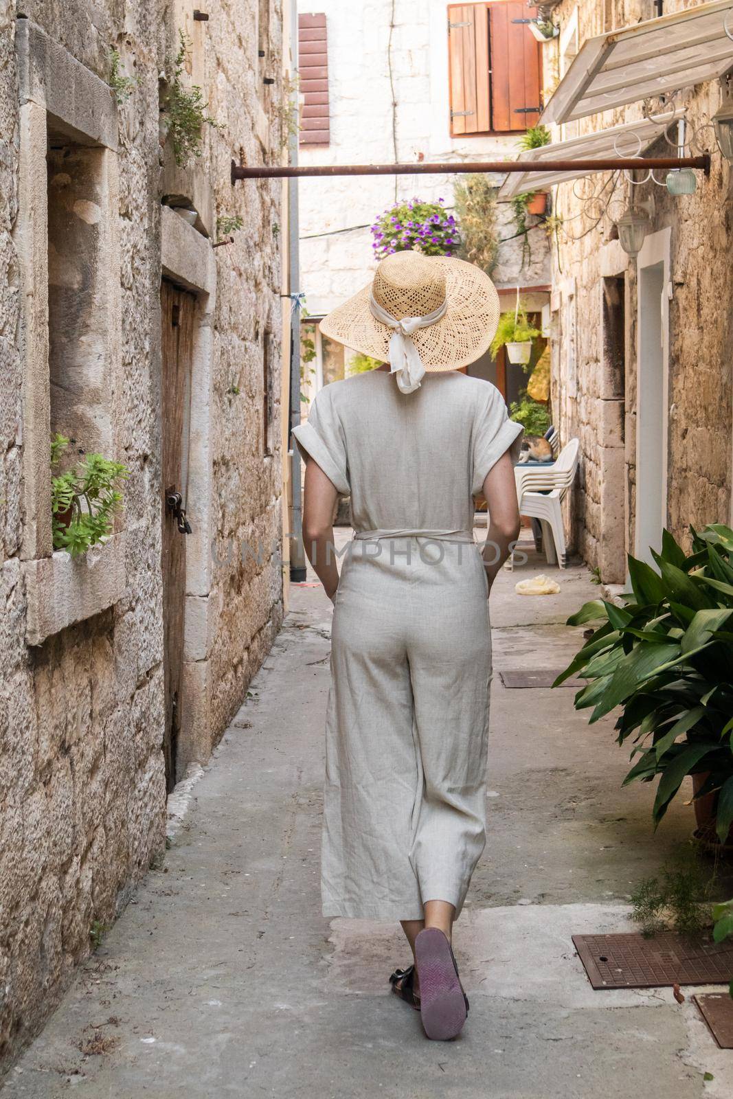 Rear view of beautiful blonde young female traveler wearing straw sun hat sightseeing and enjoying summer vacation in an old traditional costal town at Adriatic cost, Croatia by kasto