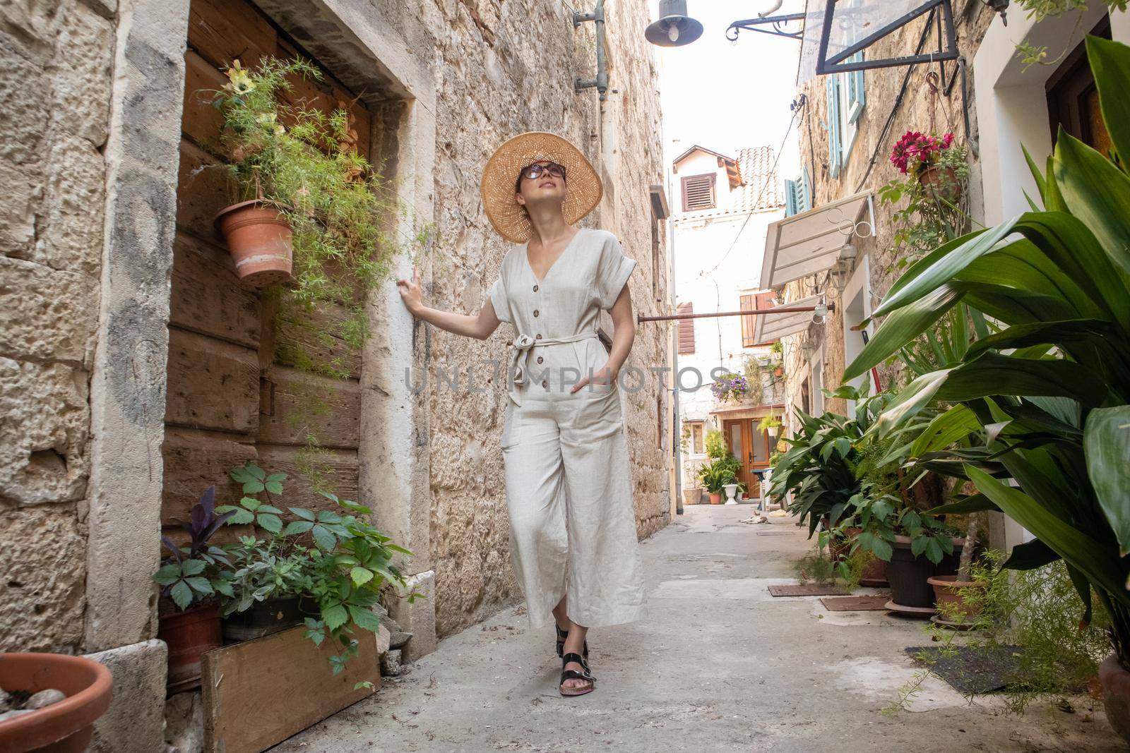 Beautiful blonde young female traveler wearing straw sun hat sightseeing and enjoying summer vacation in an old traditional costal town at Adriatic cost, Croatia.