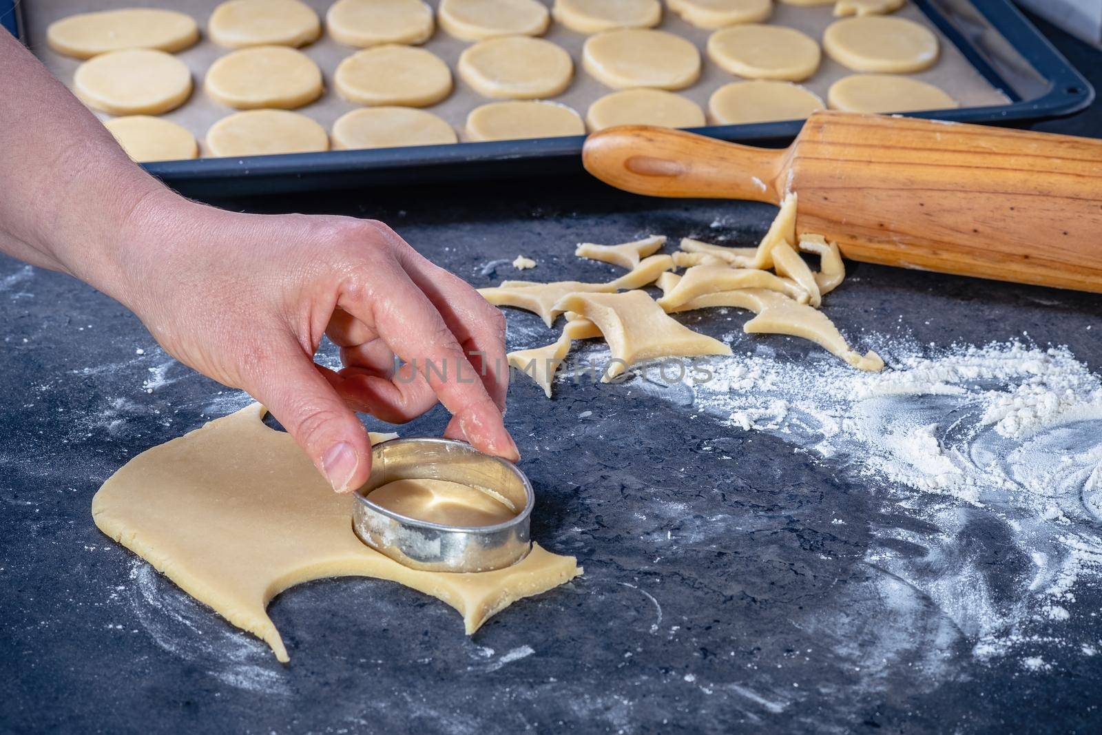  Woman prepares butter cookies at home in the kitchen, the table is sprinkled with flour, rolls out the dough, cuts out the shape, the concept of cooking festive food, christmas or easter sweets