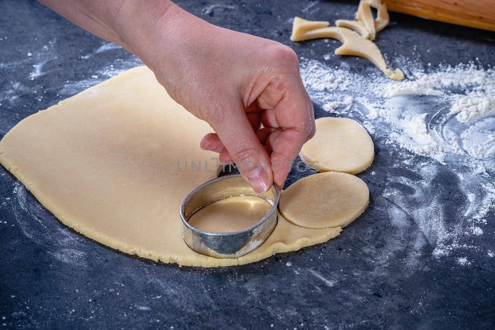  Woman prepares butter cookies at home in the kitchen, the table is sprinkled with flour, rolls out the dough, cuts out the shape, the concept of cooking festive food, christmas or easter sweets