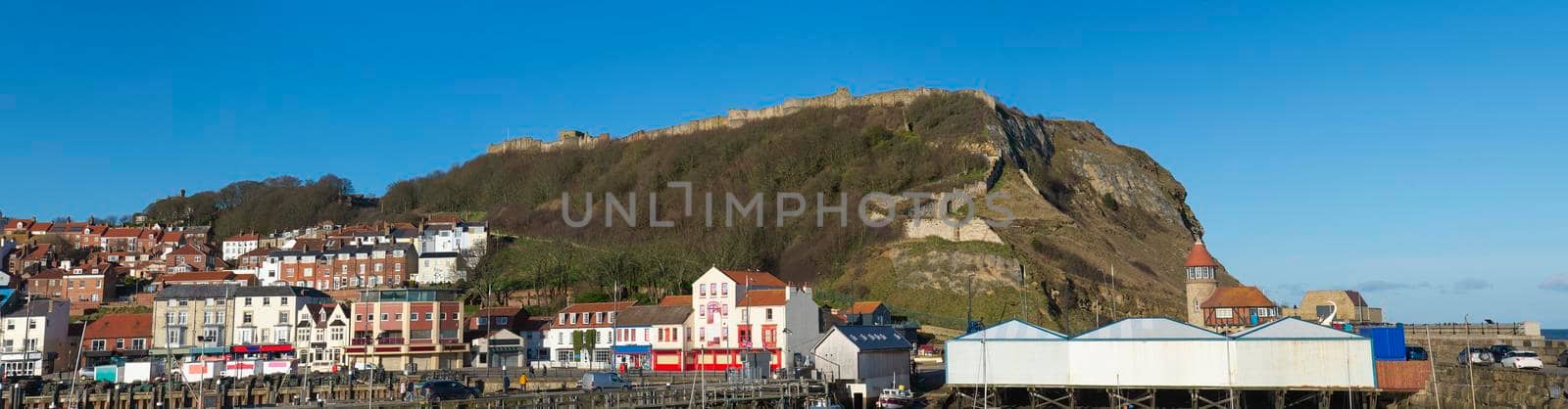 Landscape panorama view of coastal seaside town harbor front with medieval castle on hill headland