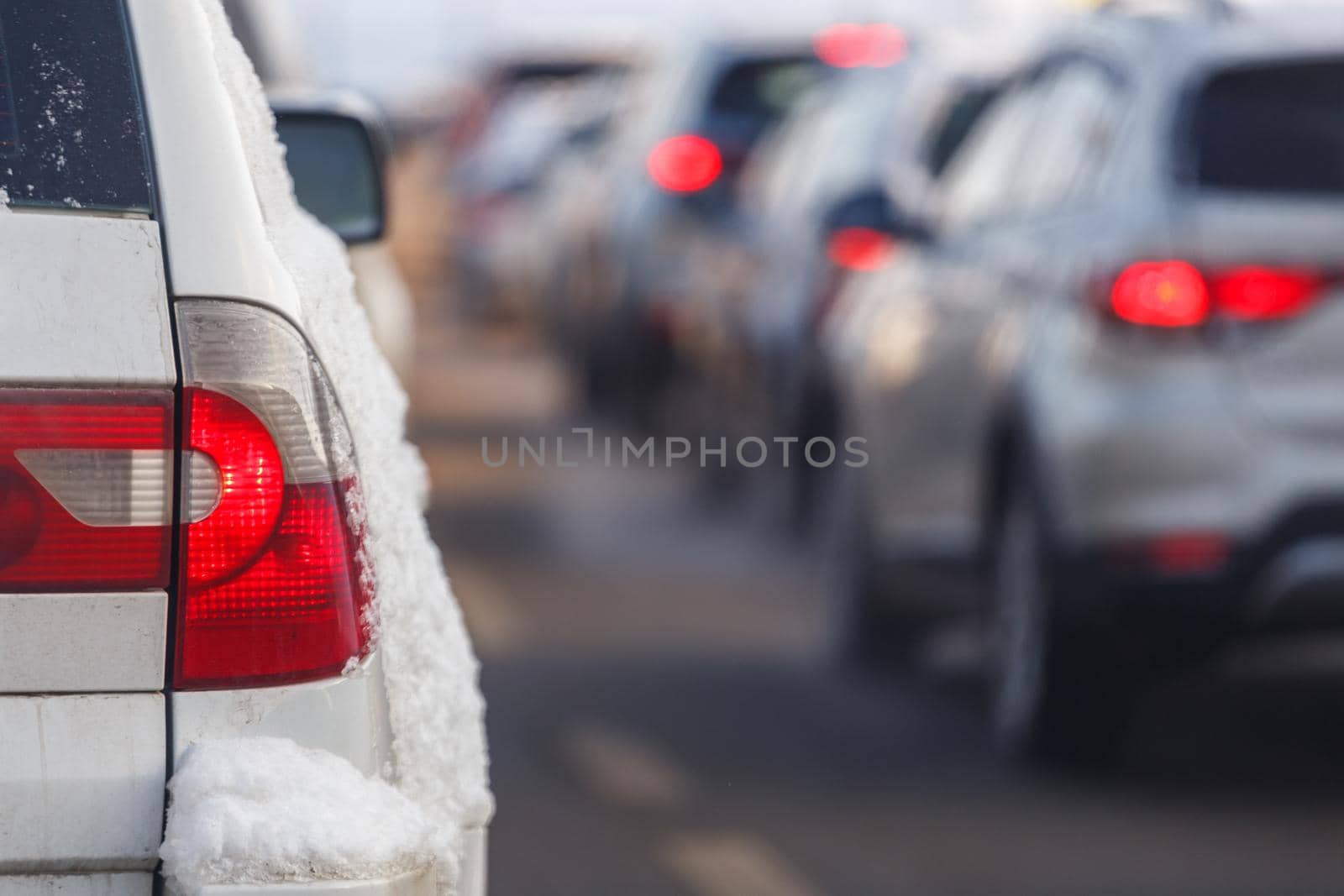 white car tail light with snow and blurry traffic in the background at winter day.