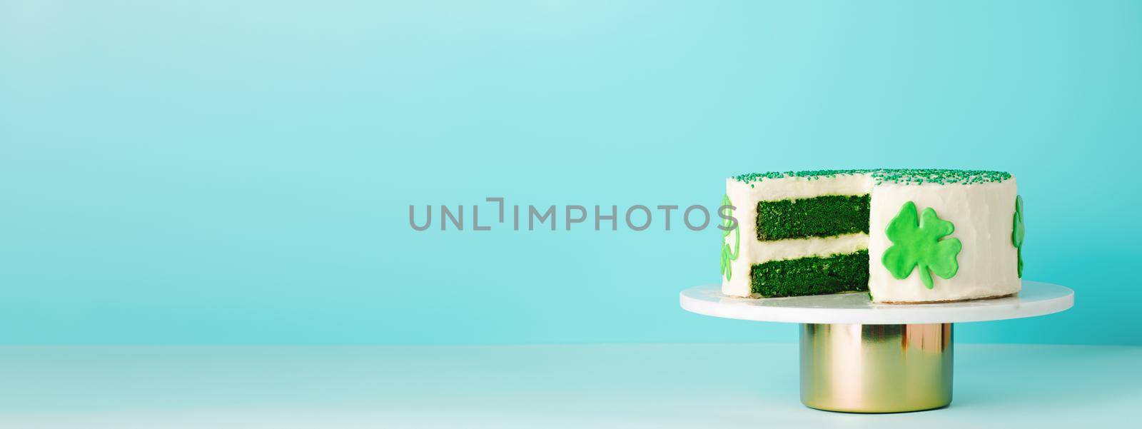 St Patricks Day sweet food concept. Green velvet cake decorated green shamrock leaves for Saint Patrick's Day party on blue background. Copy space. Long horizontal banner