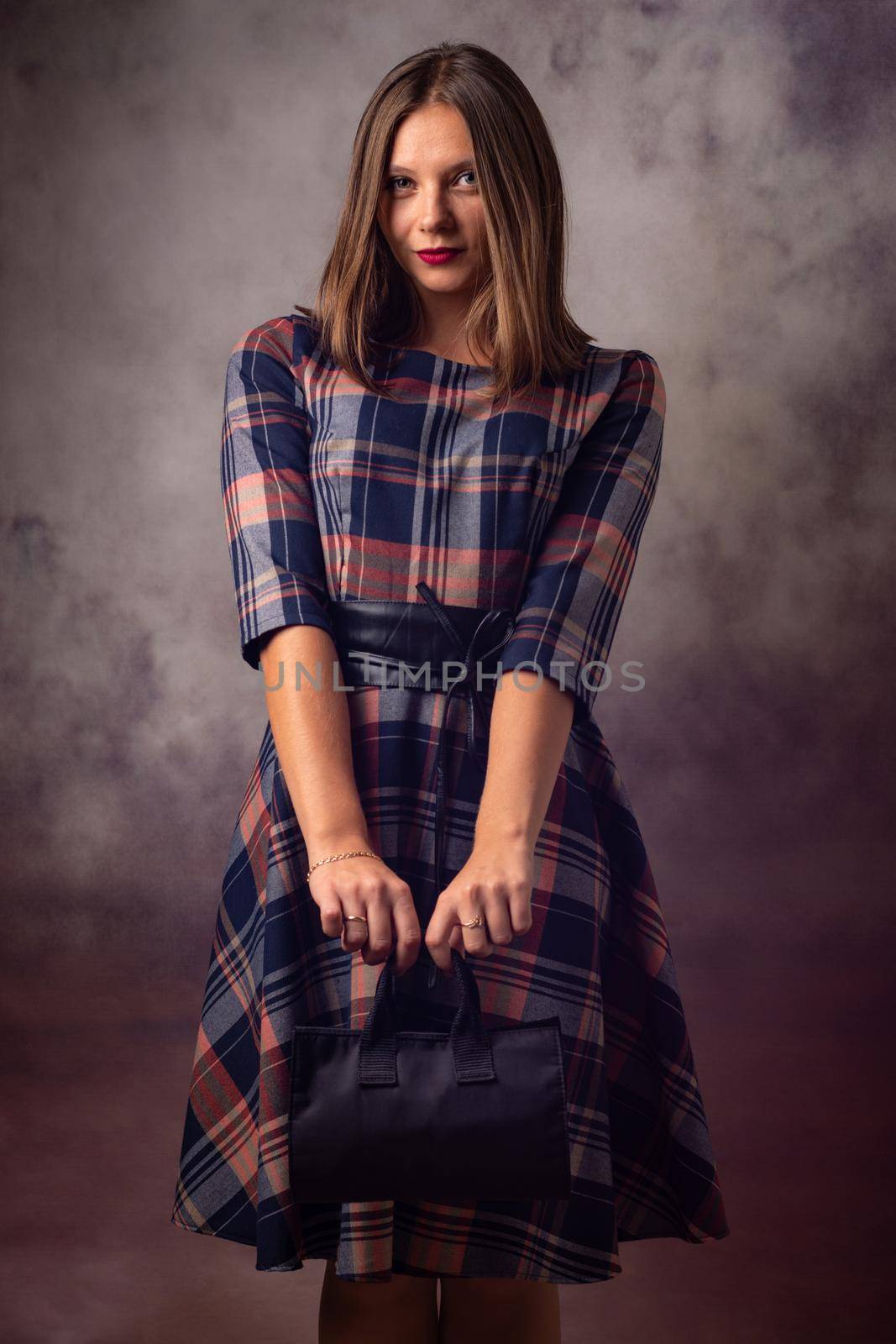 Portrait of a beautiful girl on a gray background, the girl holds a black handbag with two hands in front of her