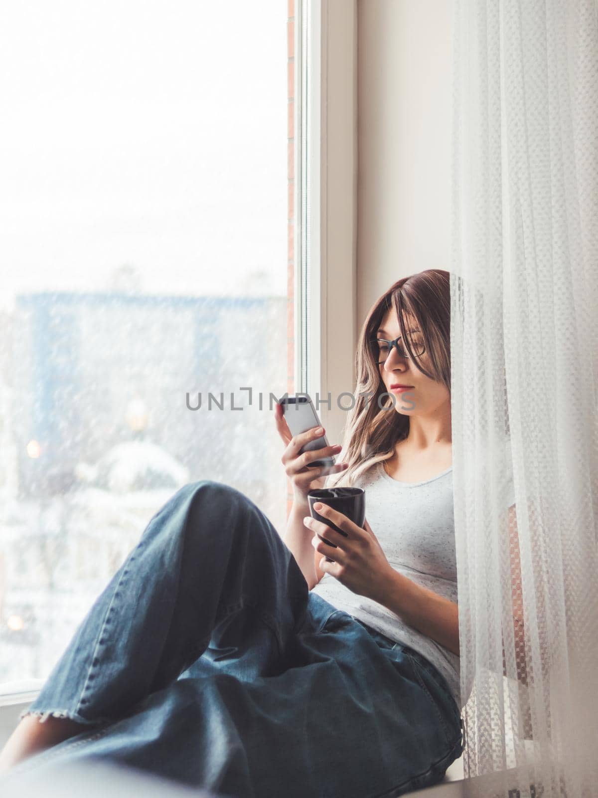 Thoughtful woman with eyeglasses and cup of hot coffee looks at her smartphone. Information in online media.