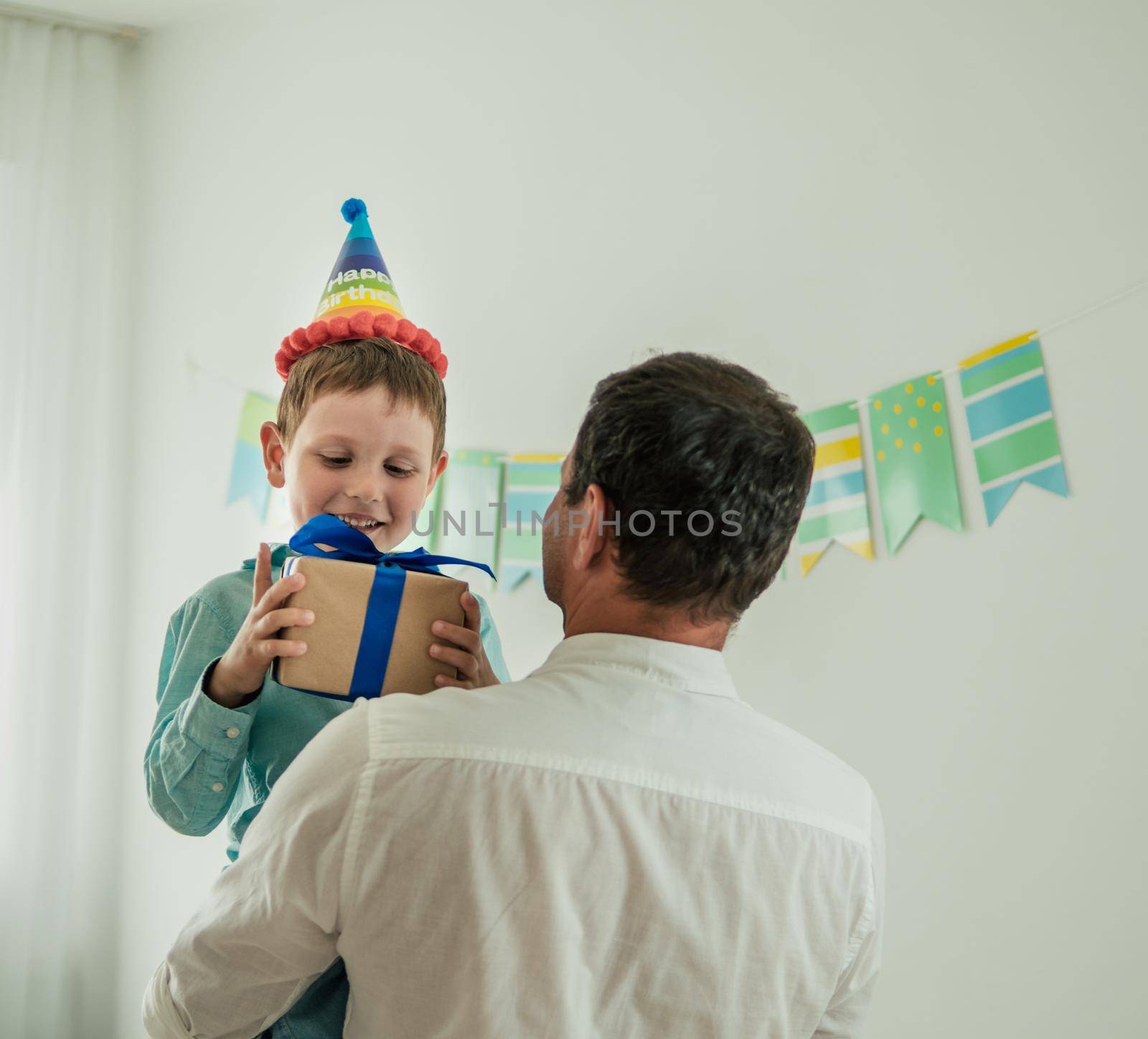 Five year old boy in his birthday hold gift box and he is in arms of dad. Happy little child hold gift box with present and looking on the box. Back view of dad. Son with birthday gift box.