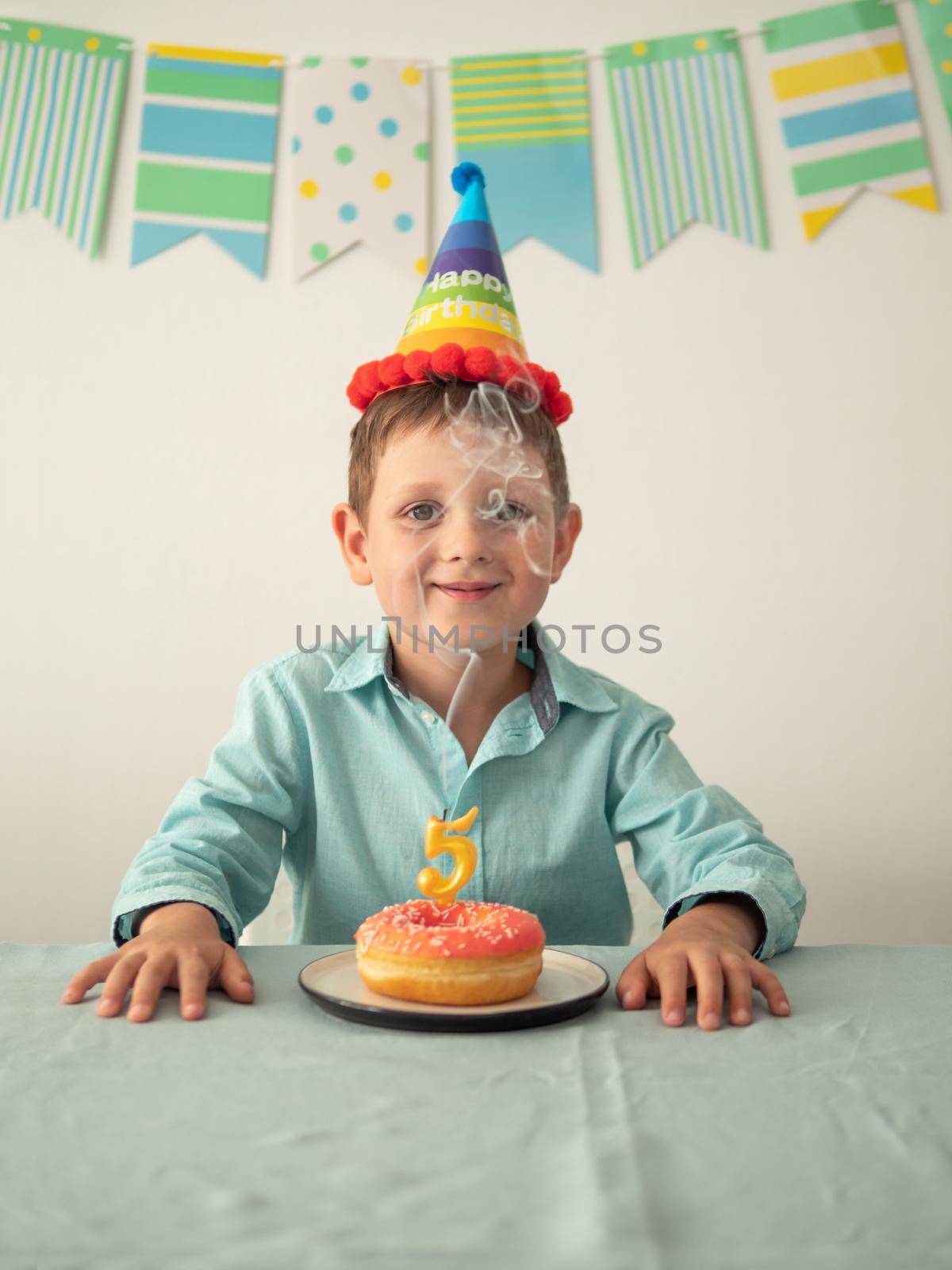 Smiling five year old boy through the smoke from extinguished candles on festie donut. Happy little child and plate with doughnut and smoke from candle. Vertical. Copy space for text or design.