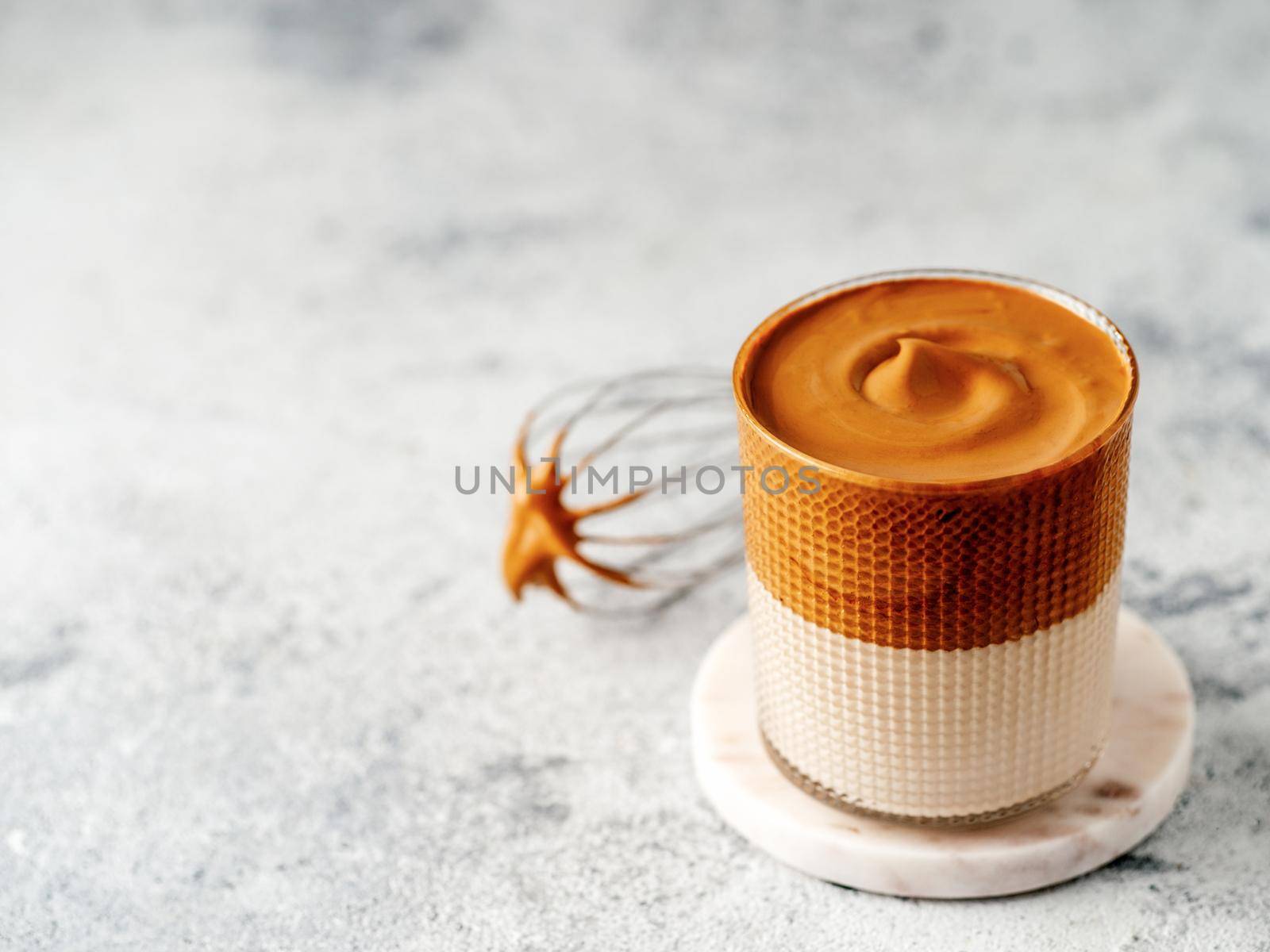 Trendy korean drink - dalgona coffee. Glass jar with cold or hot beverage - whipped instant coffee with milk and whisk on gray cement background with copy space for text or design