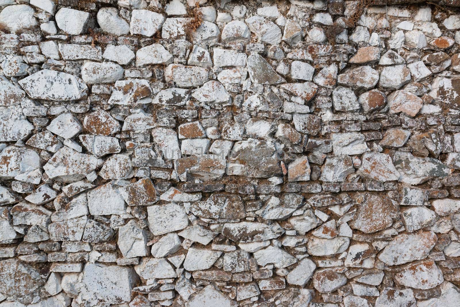 Old stone wall, painted in a faded white color and built with stones and mud