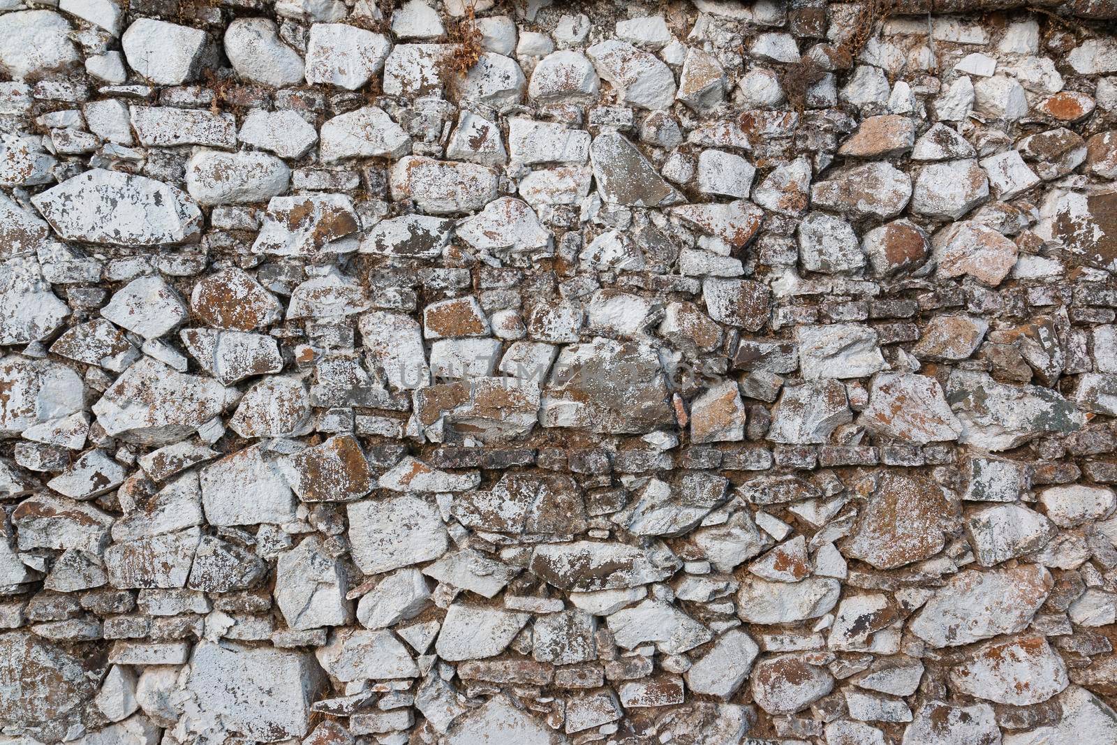 Old stone wall, painted in a faded white color and built with stones and mud