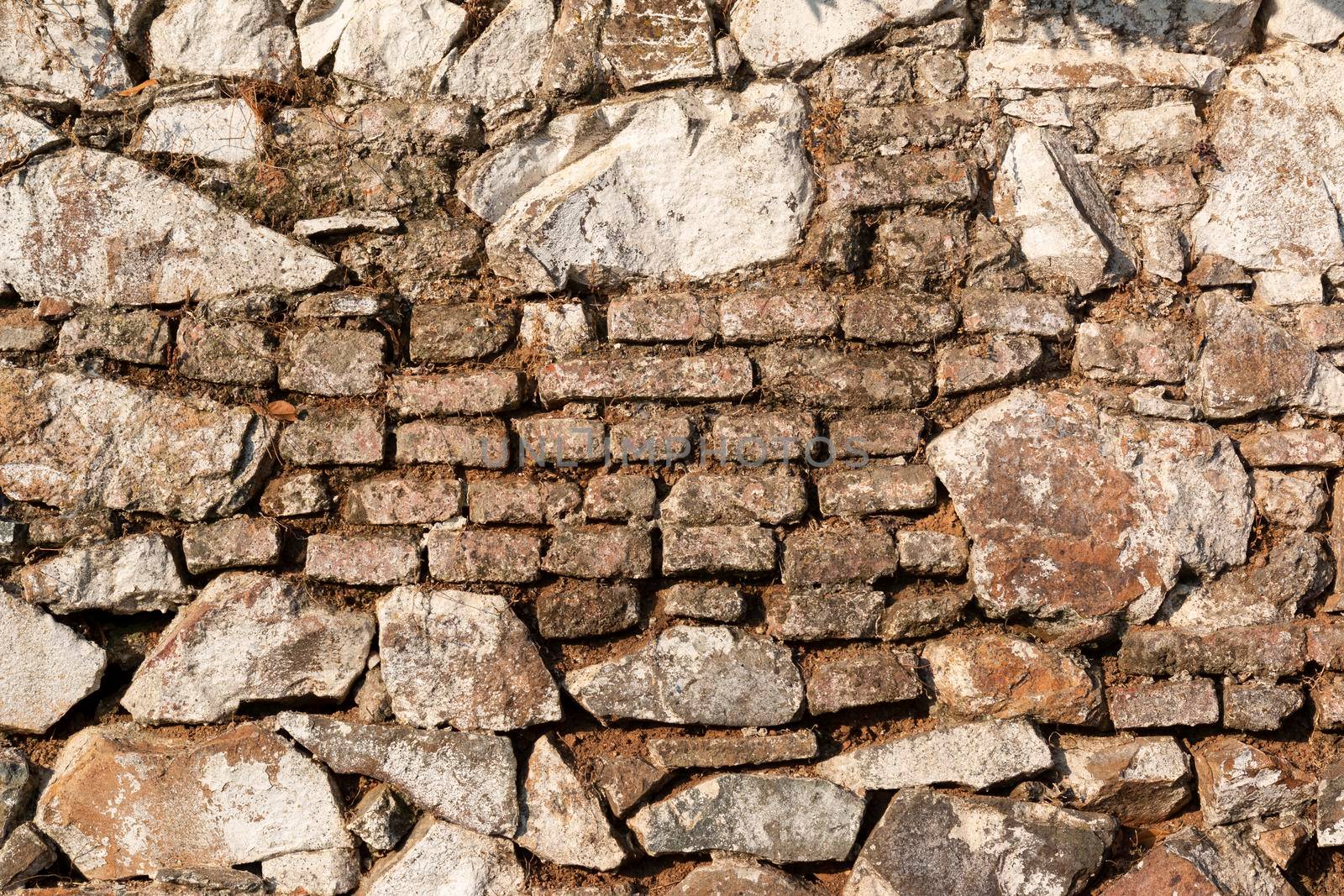 Old stone wall, painted in a faded white color and built with stones and mud