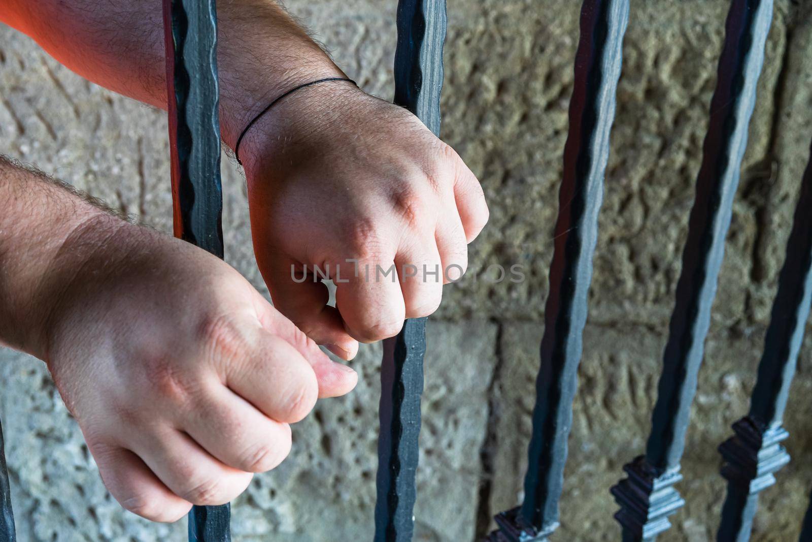 Prisoner man holding hands on jail bars. Hands on prison bars.
