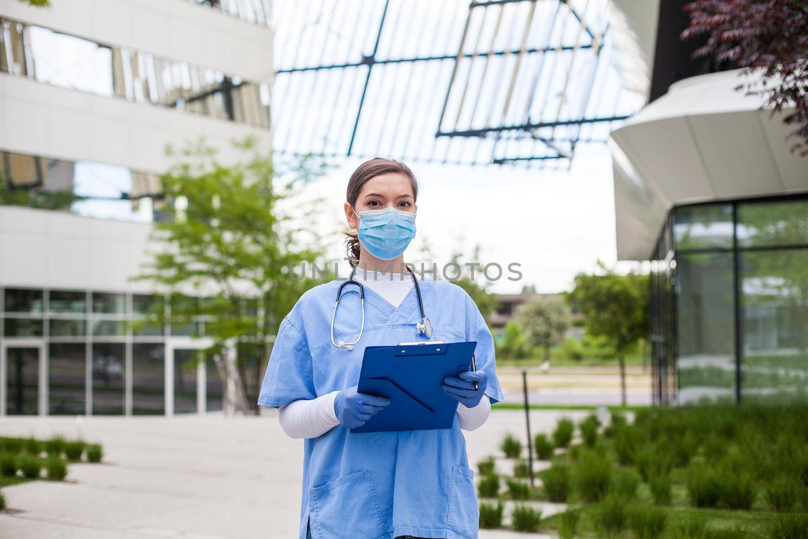 Head of care wearing personal protective equipment holding folder standing in front of nursing home,Coronavirus COVID-19 pandemic outbreak crisis,worried exhausted frontline staff,medical key worker by Plyushkin