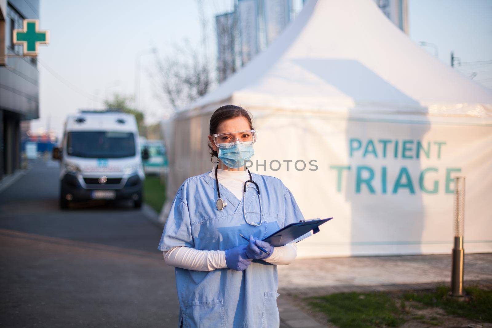 Portrait of serious female key front line worker in blue PPE uniform,standing outside EMS hospital or ICU clinic facility entrance,UK COVID-19 drive through testing site,rt-PCR Coronavirus diagnostic