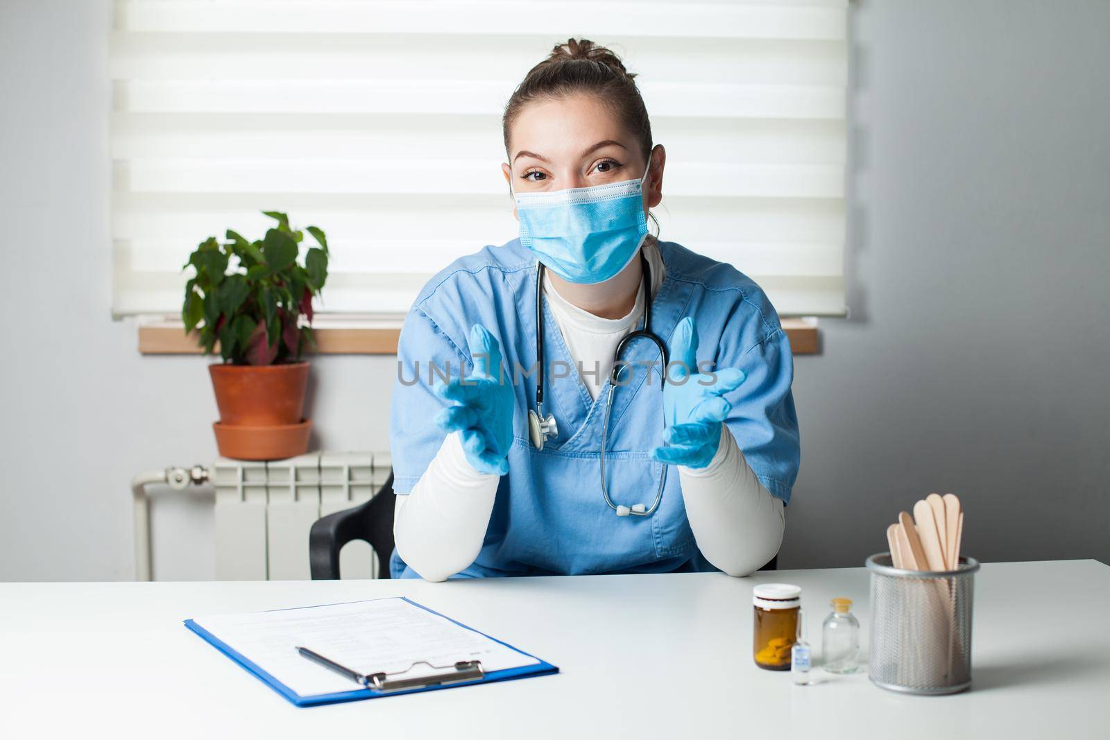 Portrait of female doctor wearing protective gloves and face mask,talking online with patient,young GP woman in blue uniform consulting person online,remote televisit assistance,telemedicine concept
