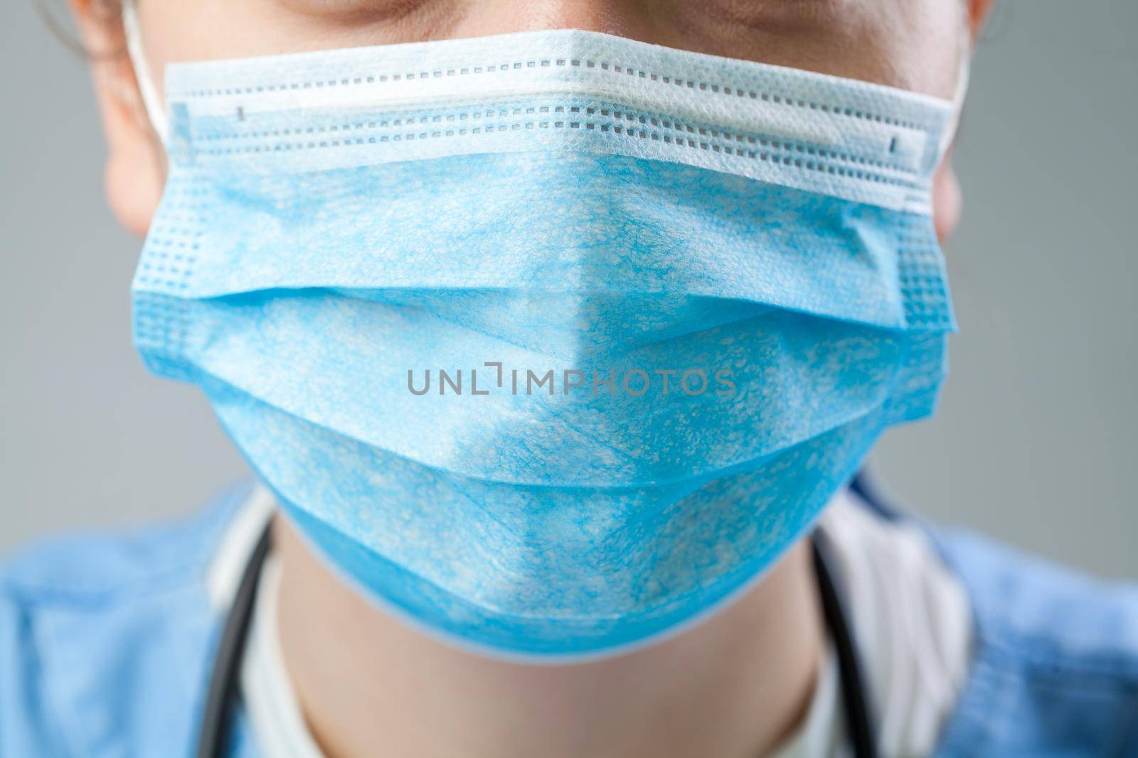Caucasian doctor or nurse wearing blue protective surgical face mask, closeup detail, Coronavirus COVID-19 global pandemic crisis outbreak causing shortage of staff and personal protective equipment
