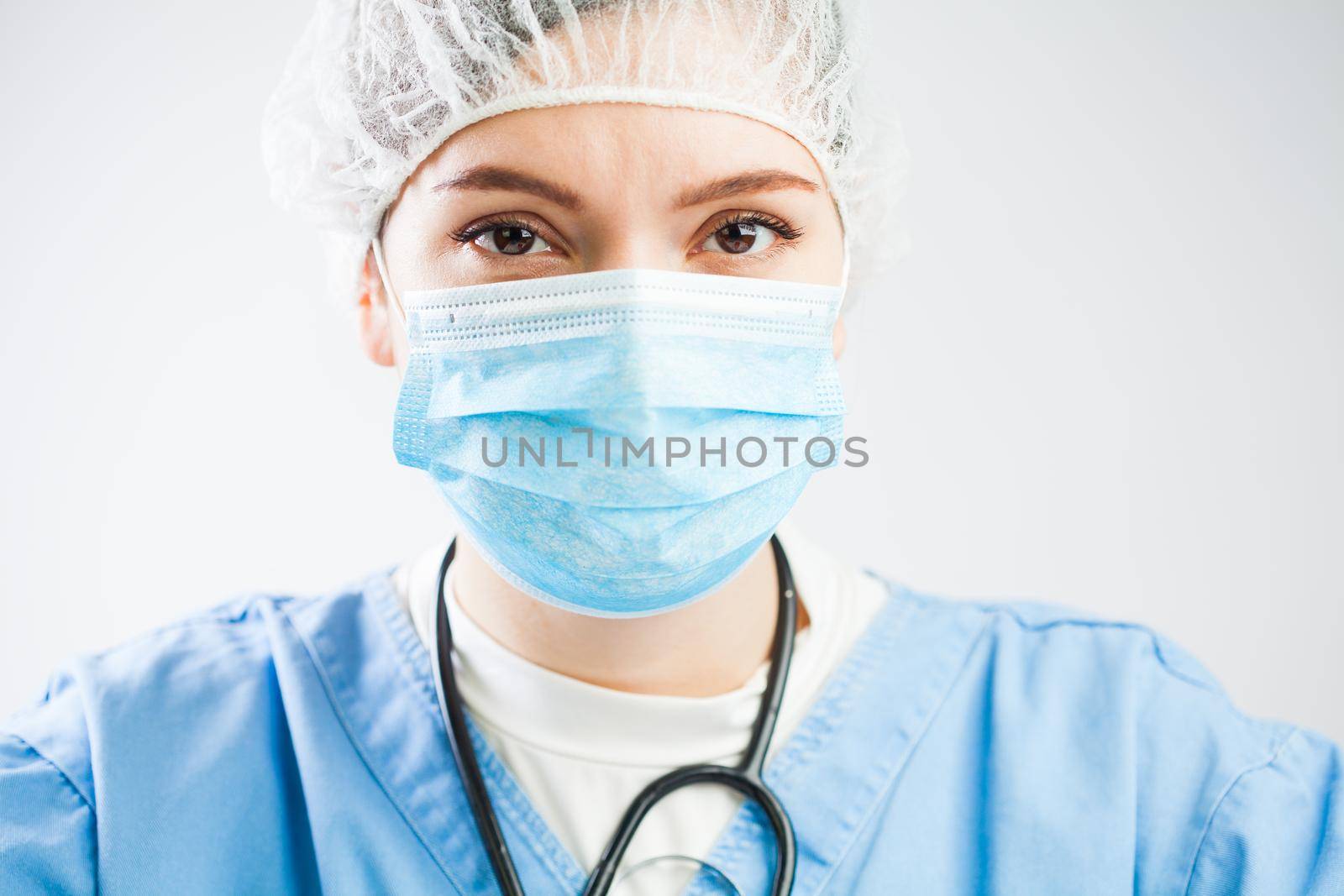 Concerned caucasian UK NHS doctor isolated on white background portrait,wearing medical PPE Personal Protective Equipment,face mask & hair cover,serious troubled look in eyes,worried stressed & tired