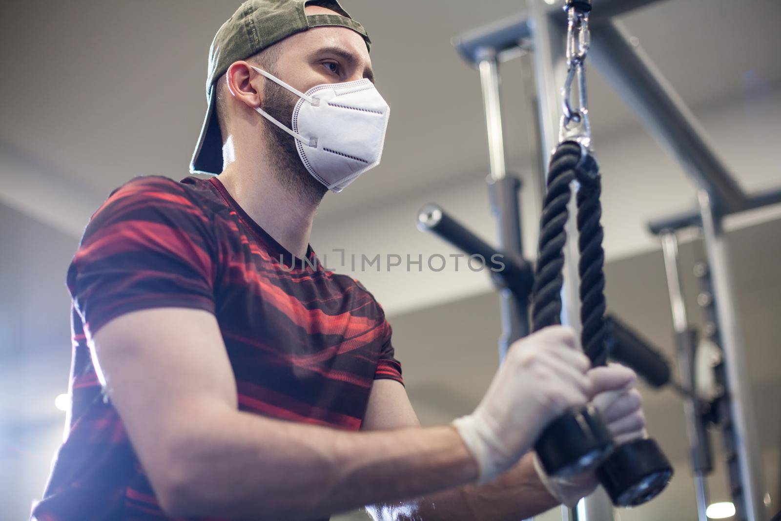 Young caucasian man working out on lat pull-down machine in re-open gym by Plyushkin