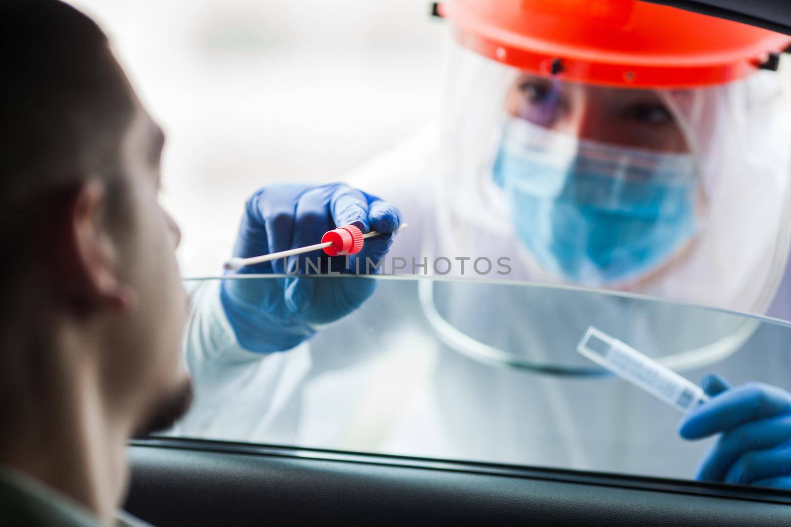 COVID-19 drive-thru patient specimen collection,female medical worker performing nasal swab on young man through vehicle window,Coronavirus point of care rt-PCR diagnostic at testing site location