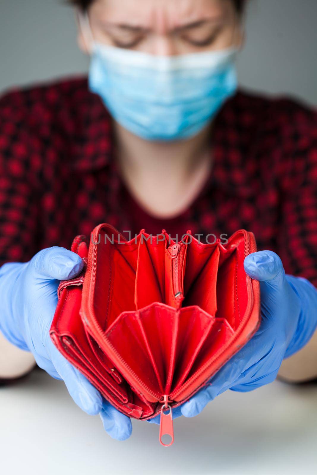 Devastated female caucasian person wearing latex gloves & medical face mask holding empty red wallet by Plyushkin