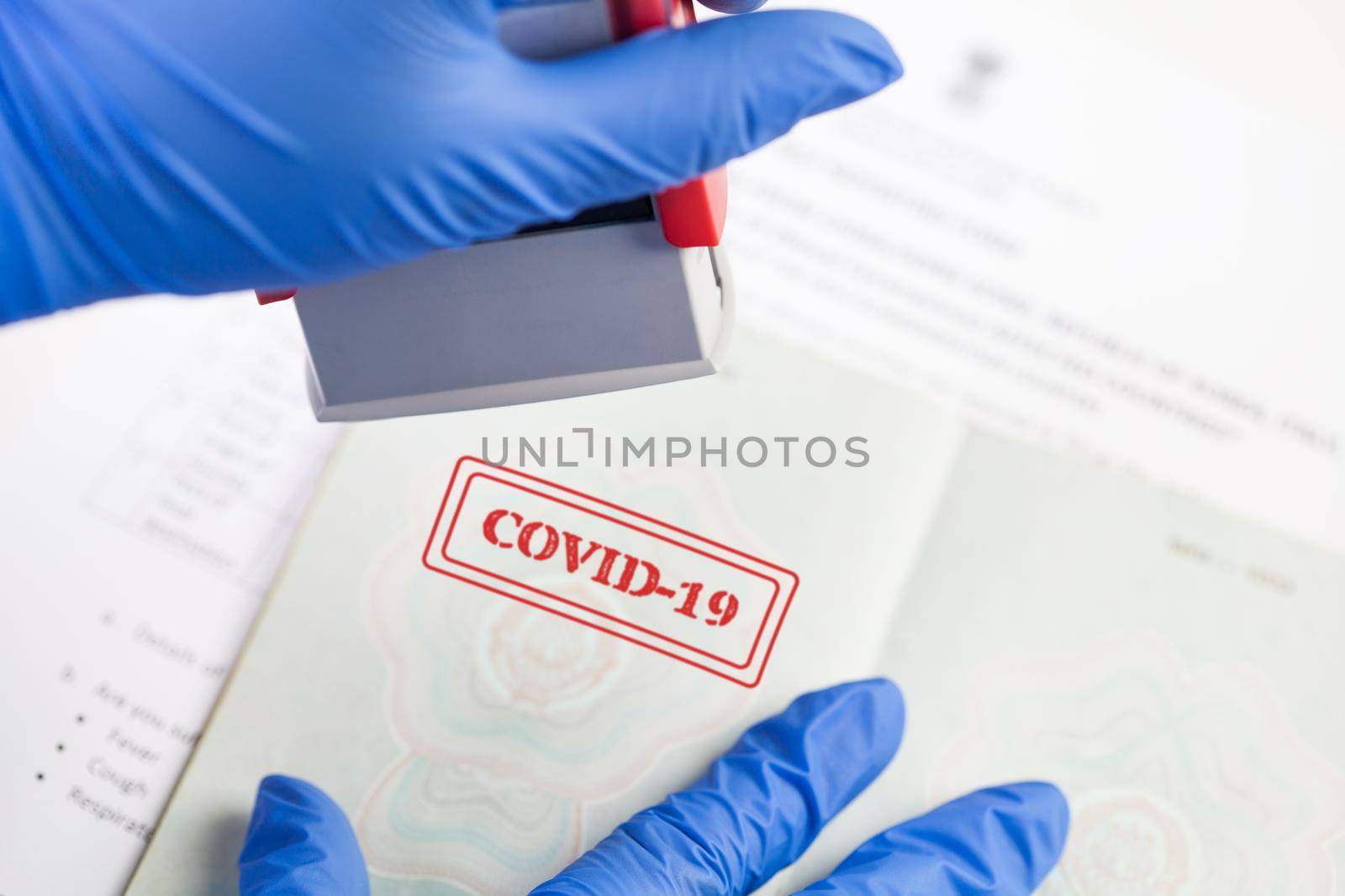 UK border security officer wearing blue protective gloves stamping COVID-19 onto document,health passport or immunity passport,risk free certificate concept,convalescent recovered Coronavirus patient