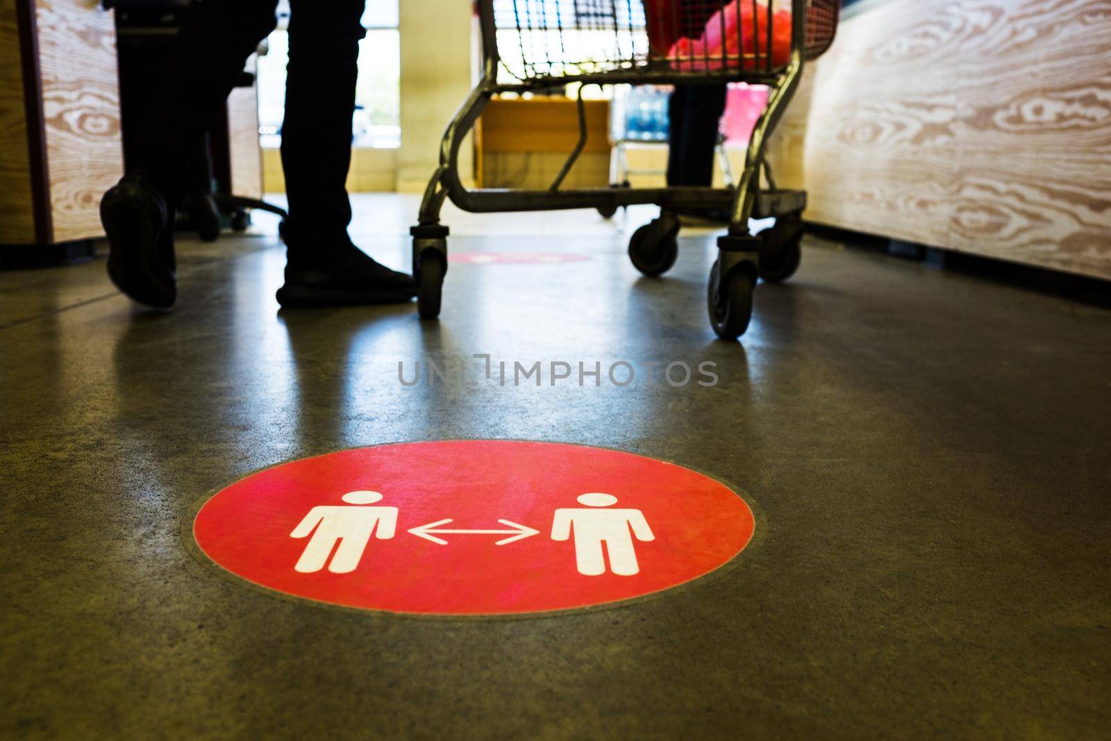 Red round circle sign printed on supermarket grocery store floor,ordering people to queue up at checkout keeping social distance,protection & prevention of spread & transfer of viruses,germs,bacteria