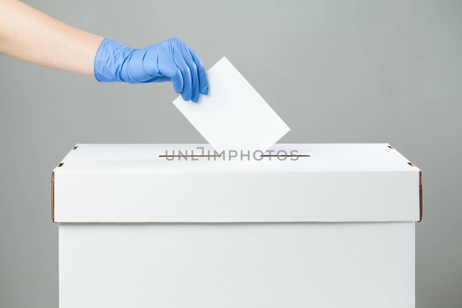 Caucasian female hand wearing blue protective latex rubber glove placing ballot paper in vote box by Plyushkin