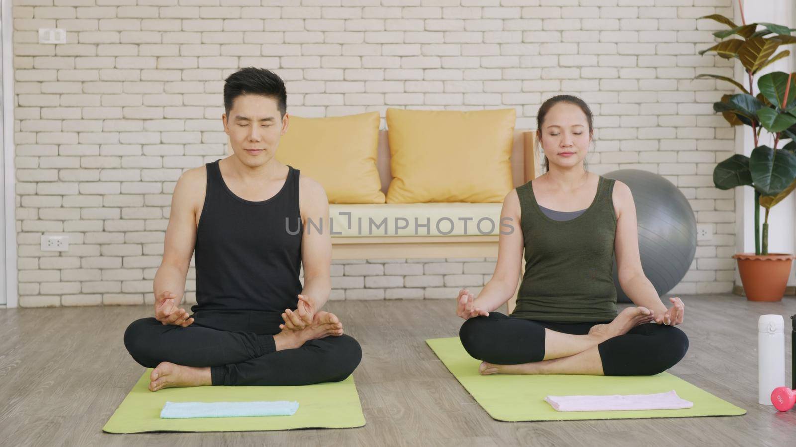 Happy Asian beautiful lifestyle family couple doing YOGA sitting meditating on lotus pose workout at home together on mat with eyes closed. Two people sport healthy concept.