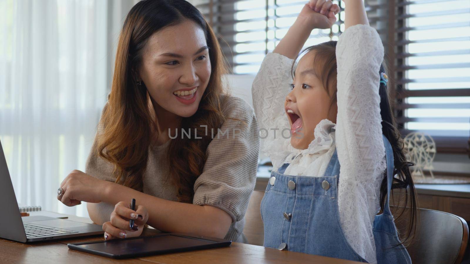 mother working with laptop computer at home and help daughter doing homework by Sorapop