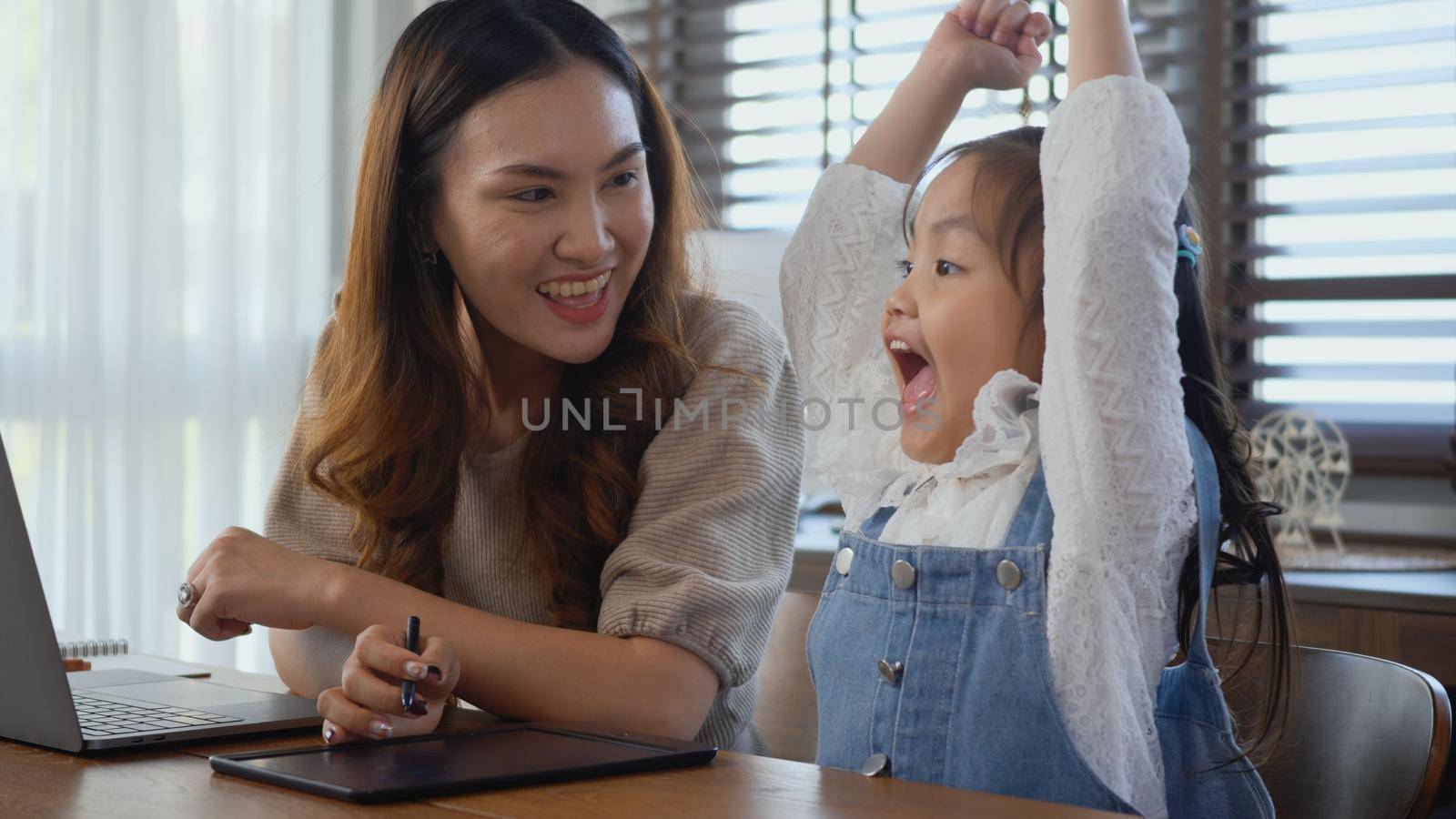 Asian young mother working with laptop computer at home and help daughter doing homework, Single mom freelancer work from home and helping his girl kid teaching homework on desk