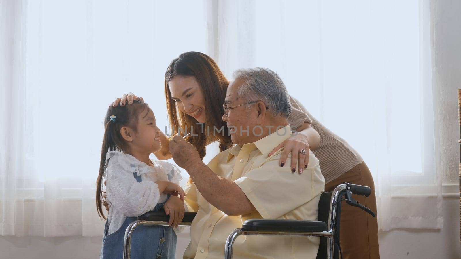 Asian happy disabled elderly in wheelchair with daughter and granddaughter smiling playing together in living room at home, family visit to support old senior man