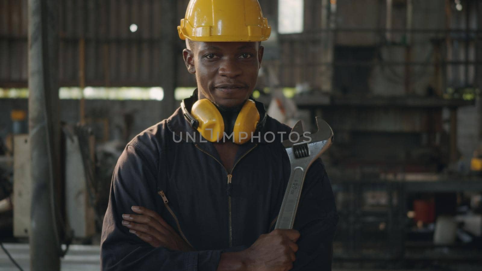 Portrait American industrial black young worker man smiling with yellow helmet in front machine, Engineer standing holding wrench tools and arms crossed at work in the industry factory.