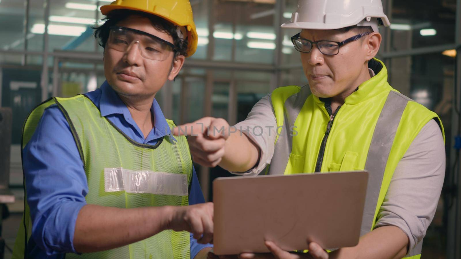 Two factory industrial workers technician or engineer and manager wear uniforms safety feeling upset with the engine machine of the factory arguing about planning procedure of work on laptop computer