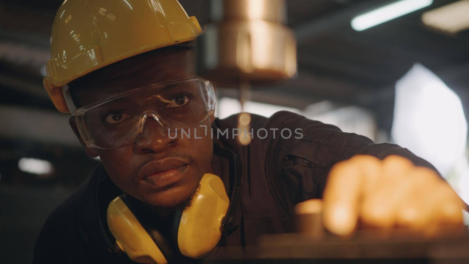 worker man with yellow helmet and ear protection manual rotating on drill machine by Sorapop