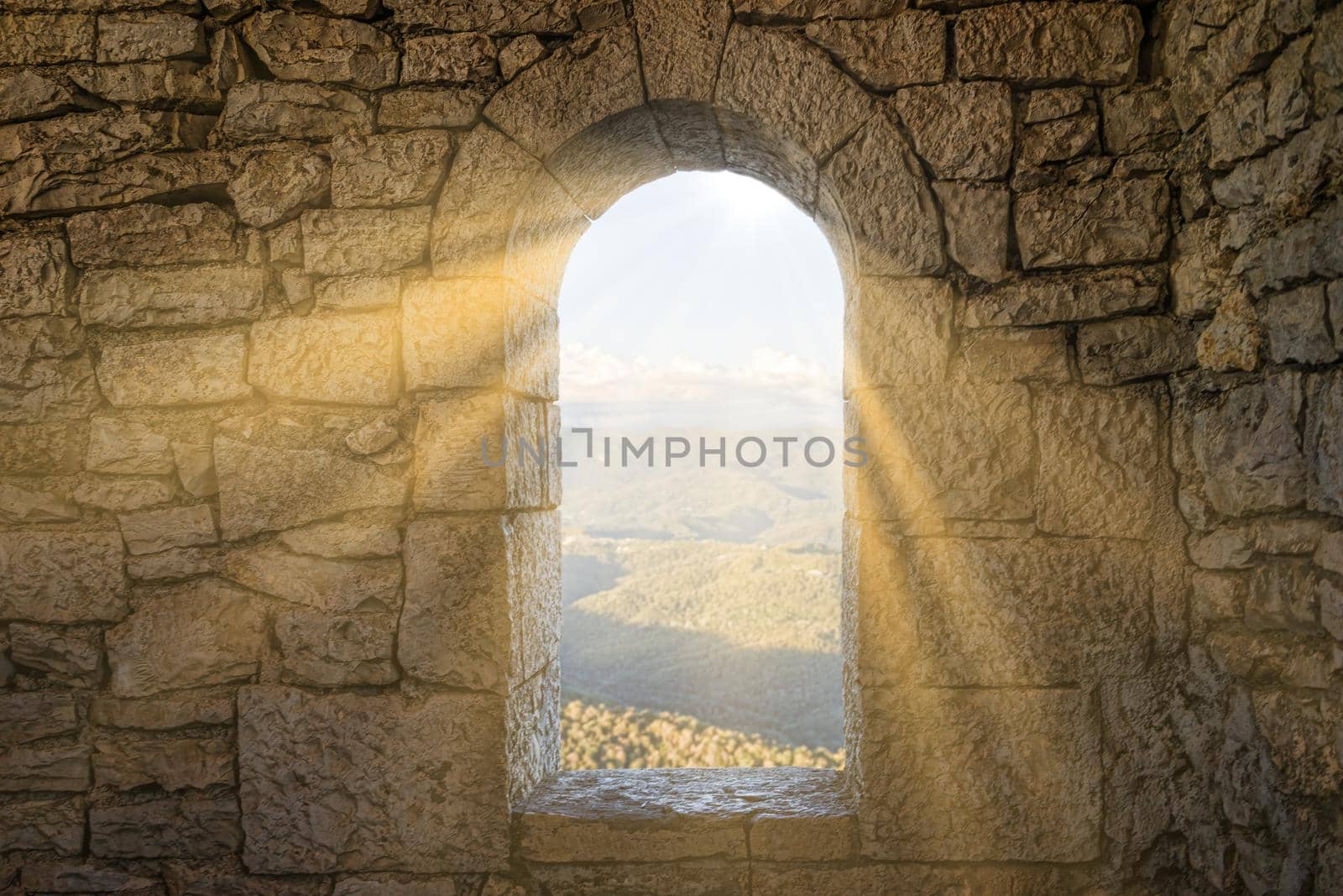 A window in a stone wall overlooking a mountain landscape.