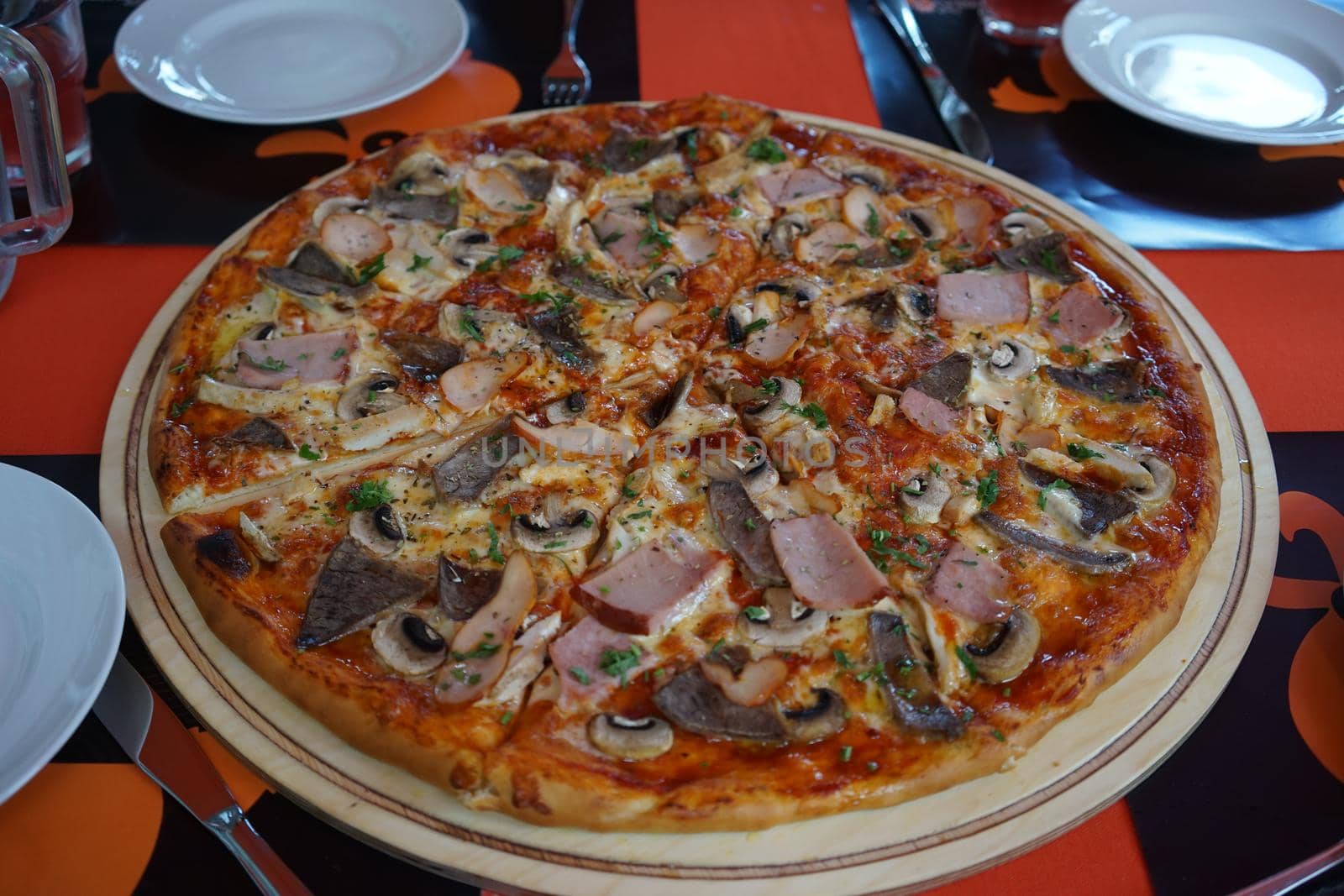 a huge pizza with various fillings standing on a red table surrounded by white tableware