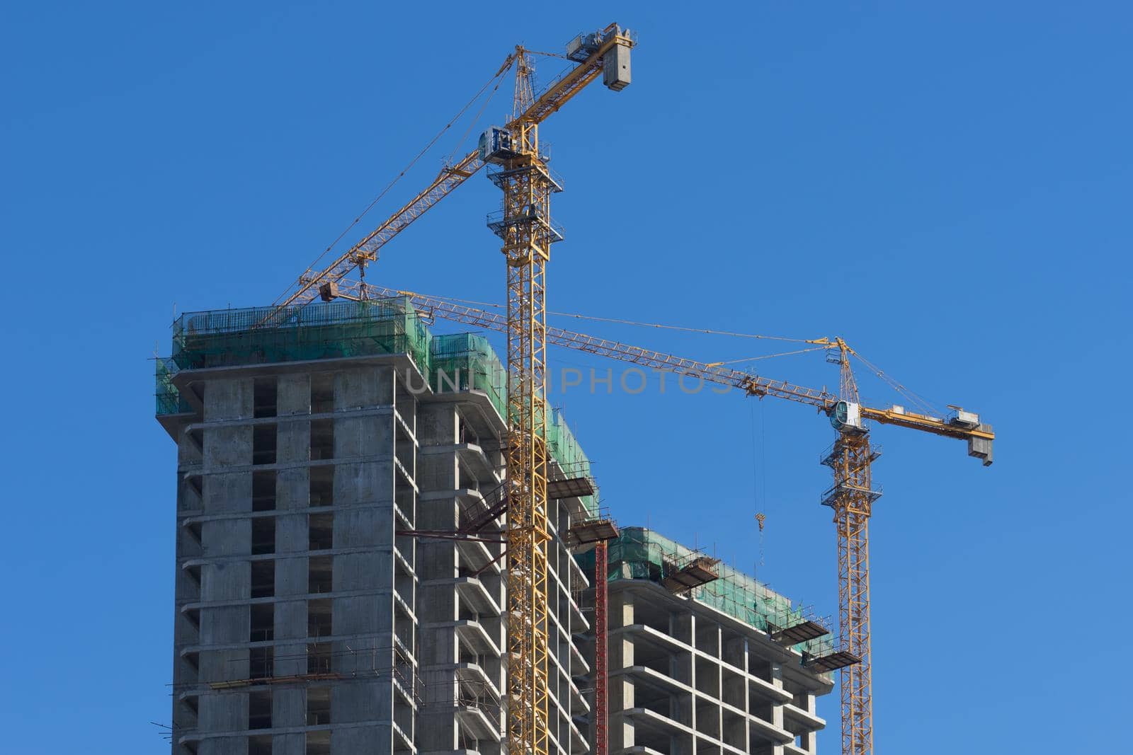 Urban landscape with views of the house under construction and cranes against the blue sky.