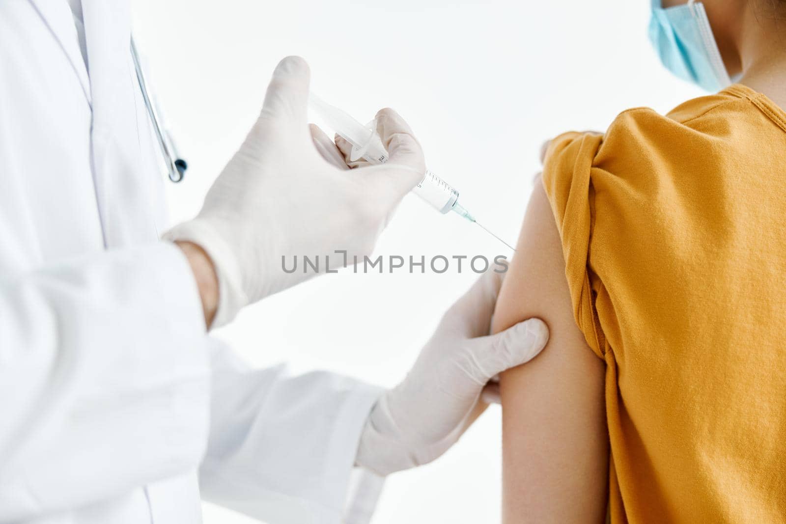 doctor injecting vaccine into patient's shoulder in medical mask in hospital back view. High quality photo