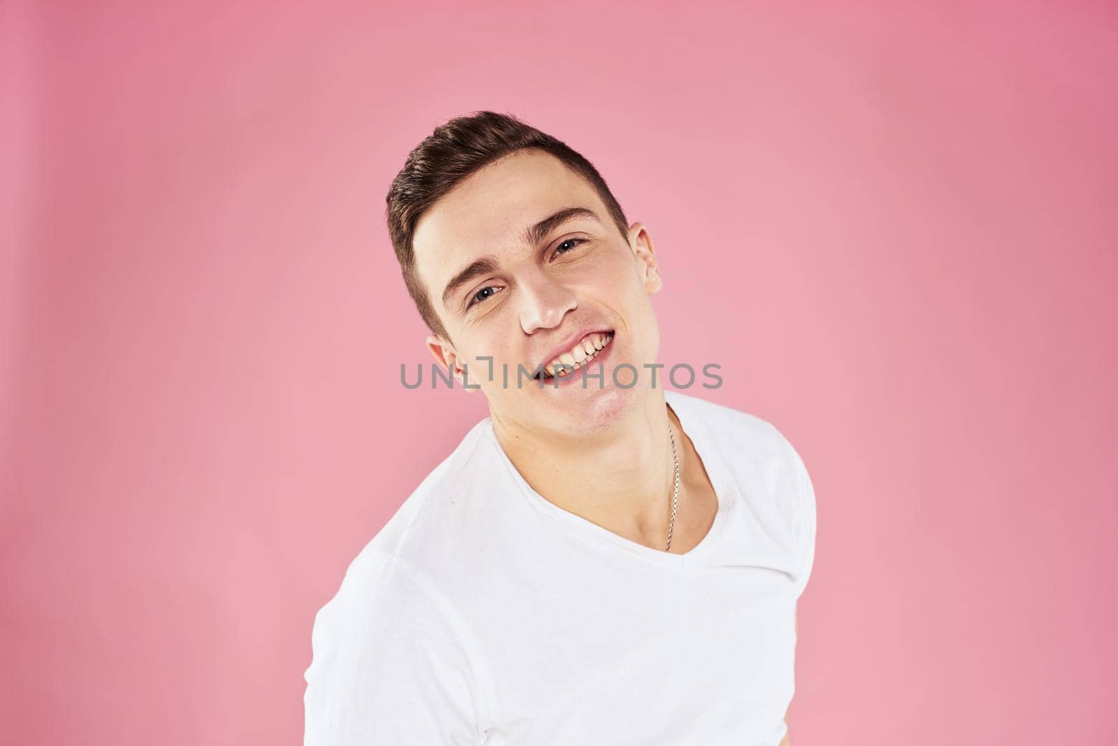 A man in a white t-shirt gestures with his hands emotions pink background studio cropped view. High quality photo