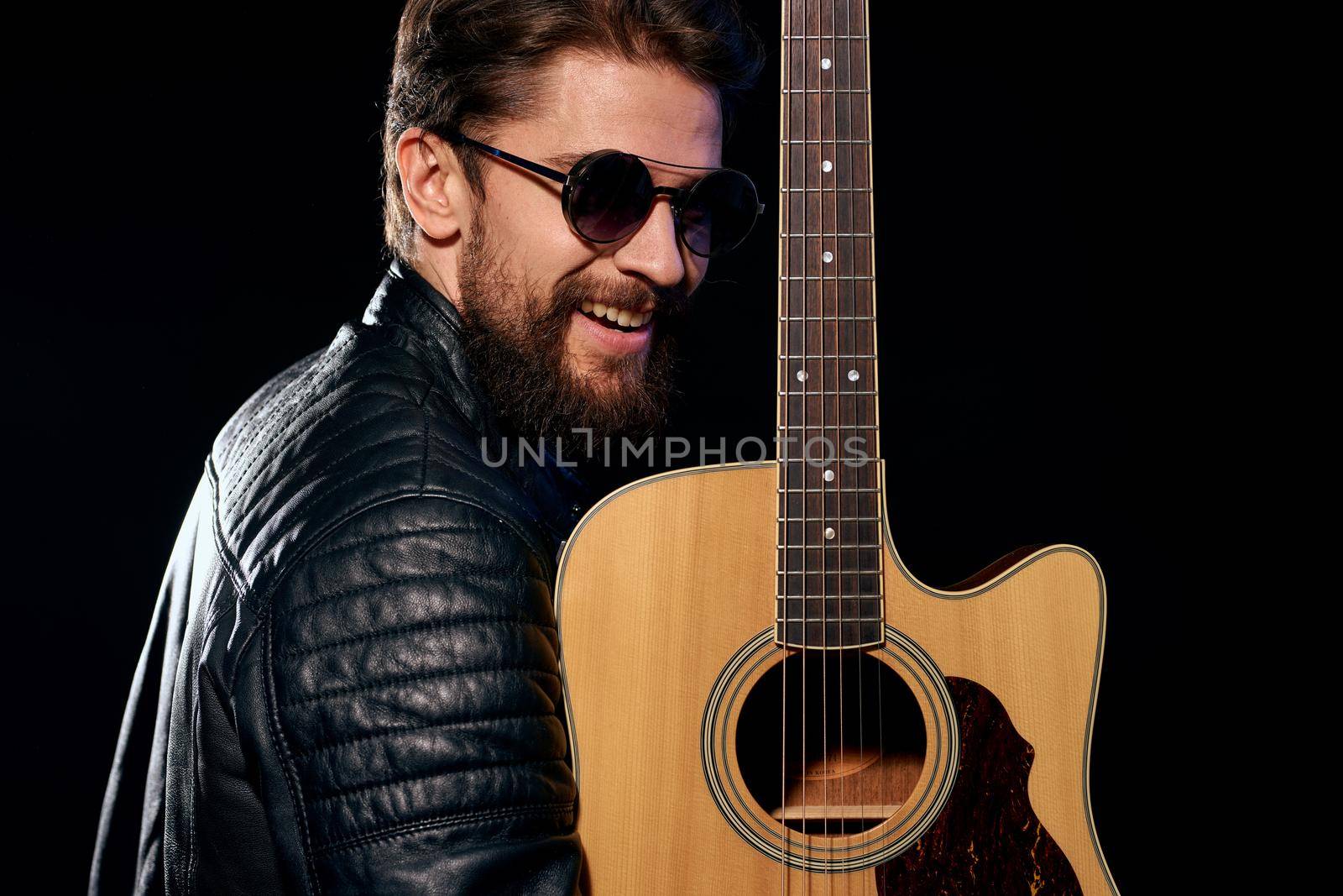 A man with a guitar in his hands leather jacket music performance rock star modern style dark background. High quality photo