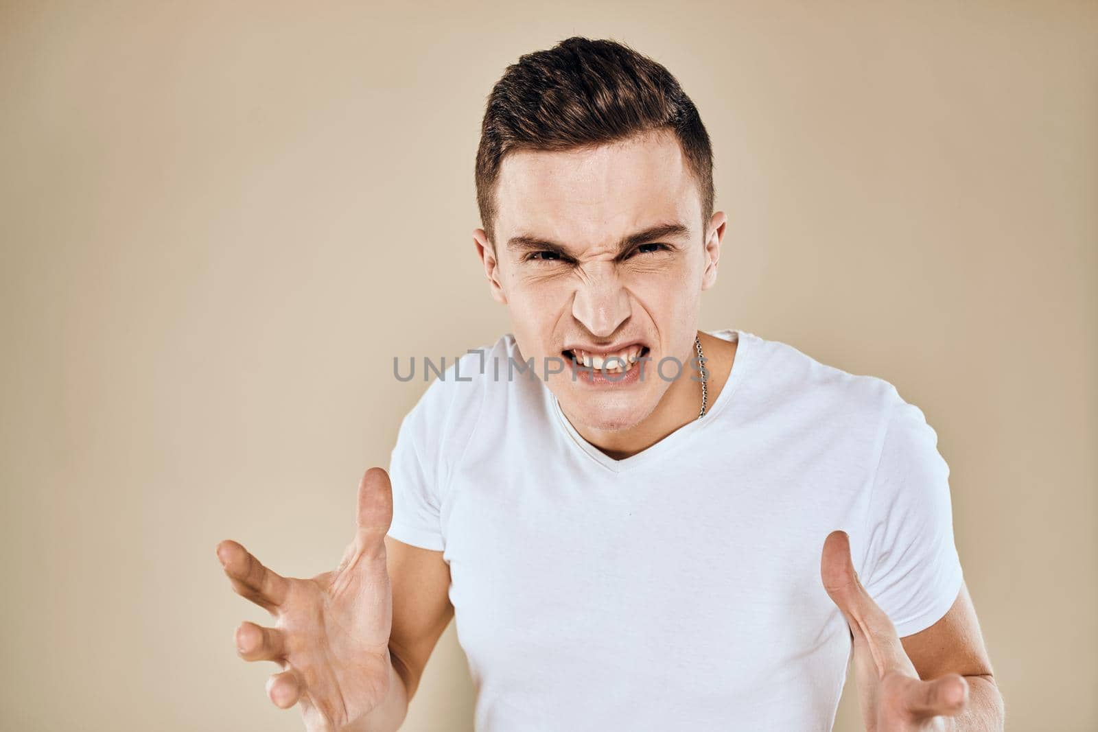 Man with displeased facial expression emotions white t-shirt gestures with hands beige background by SHOTPRIME