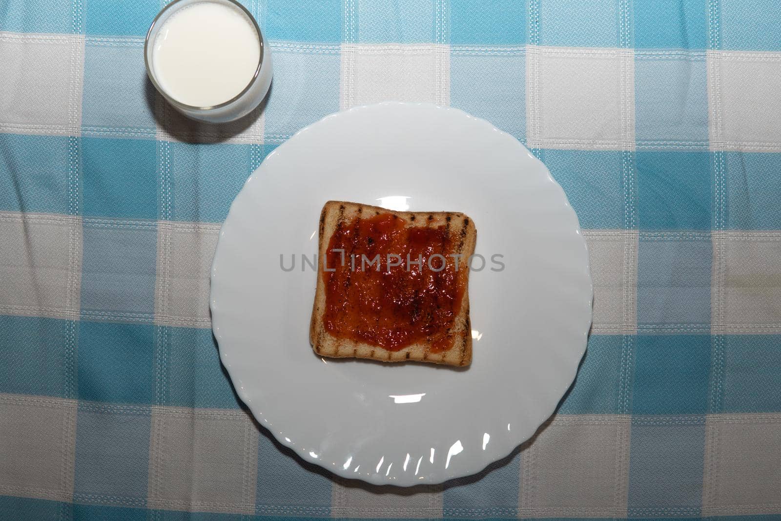 Toasted sliced bread with strawberry jam, a glass of milk and blue checkered fondant.