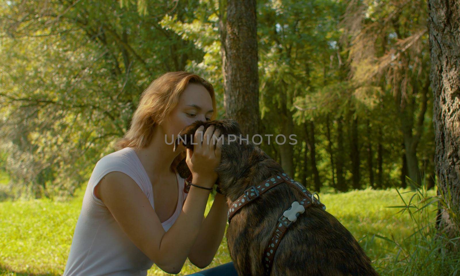 Attractive smiling woman kissing her nice dog. Young attractive lady and her dog on the stroll in the park.