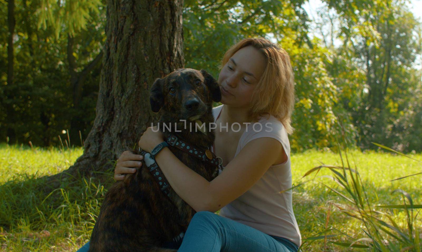 Attractive smiling woman hugging her nice dog. Young attractive lady and her dog on the stroll in the park.