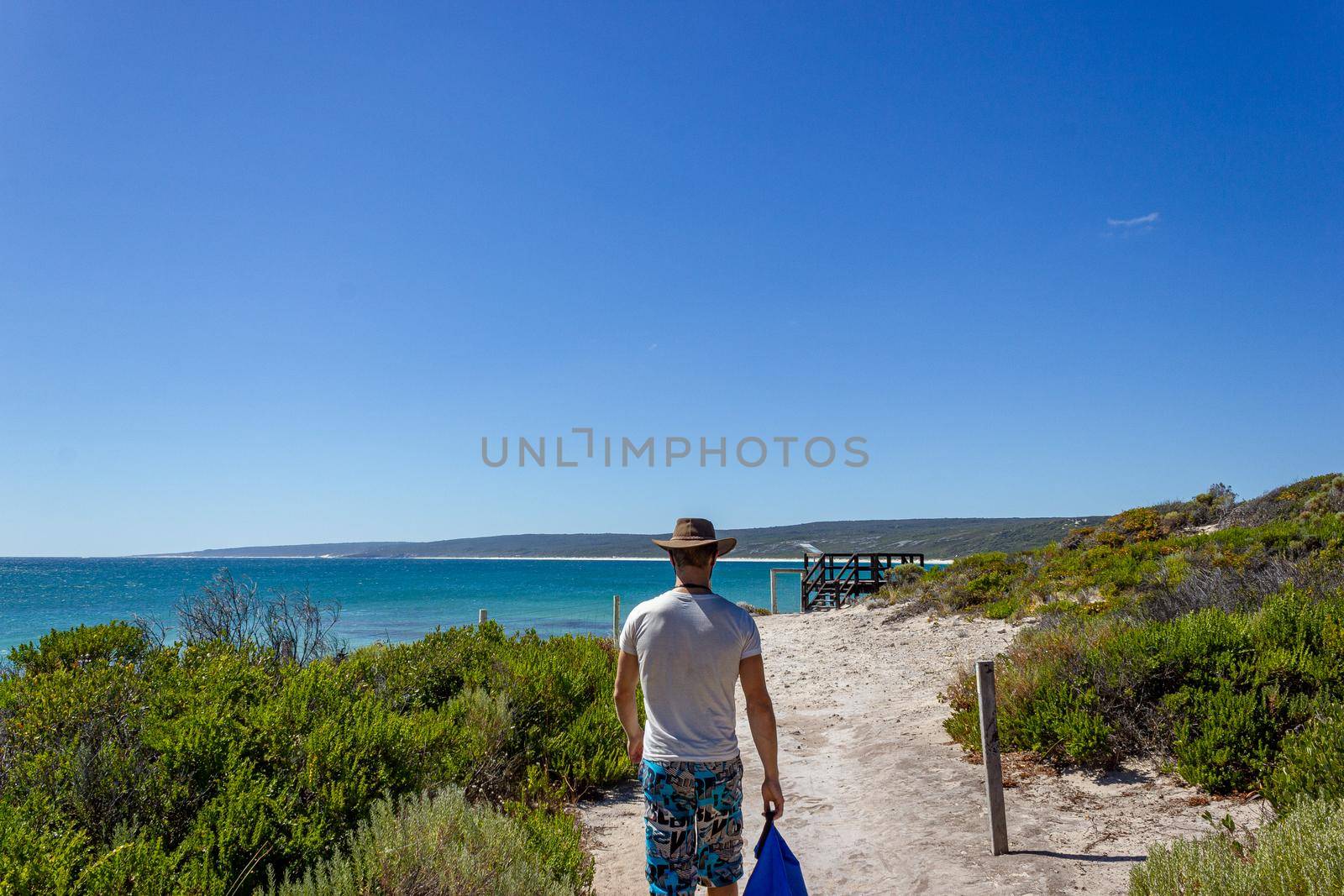 young caucasian man with a blue bag walking down a pathway to Hamelin Beach. This Beach is famous for his stingrays, Hamelin Beach, Western Australia by bettercallcurry