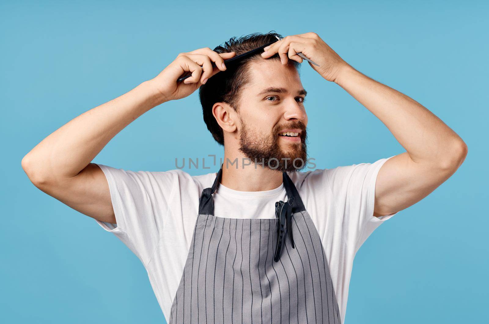 professional hairdresser man in a gray apron does his hair on a blue background and scissors comb. High quality photo