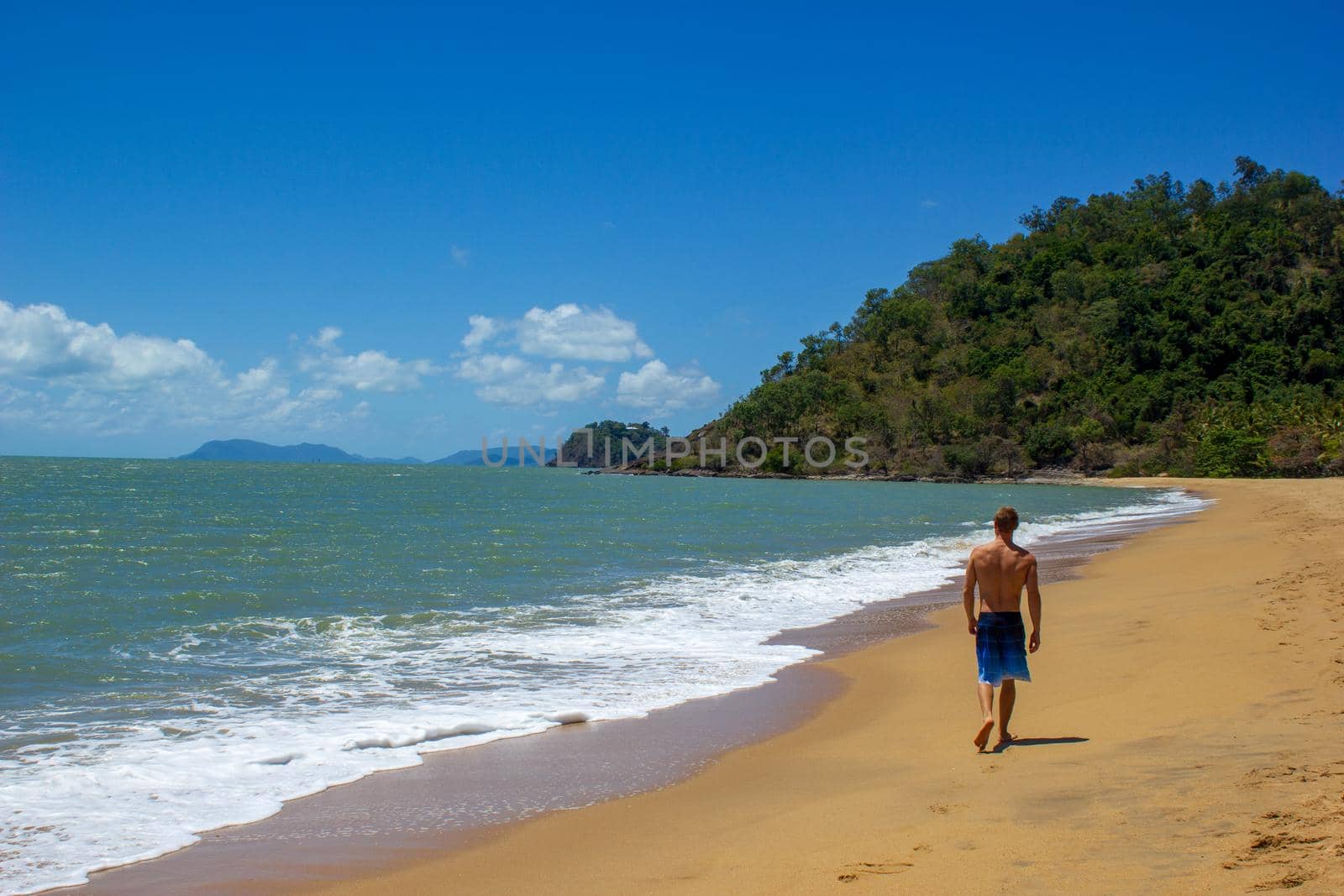 Muscular caucasian man walking on the beach as ocean waves crash behind him, cape tribulation, queensland, australia by bettercallcurry