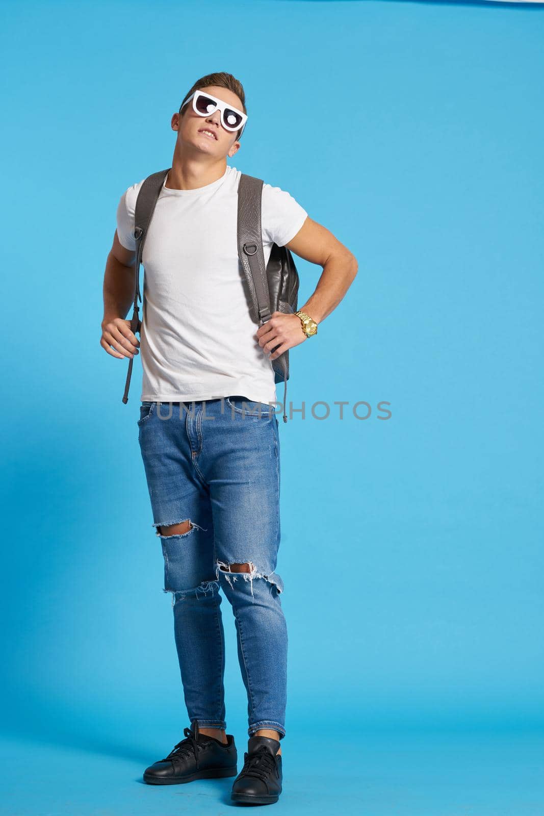 Cheerful young guy with backpack studio blue background. High quality photo