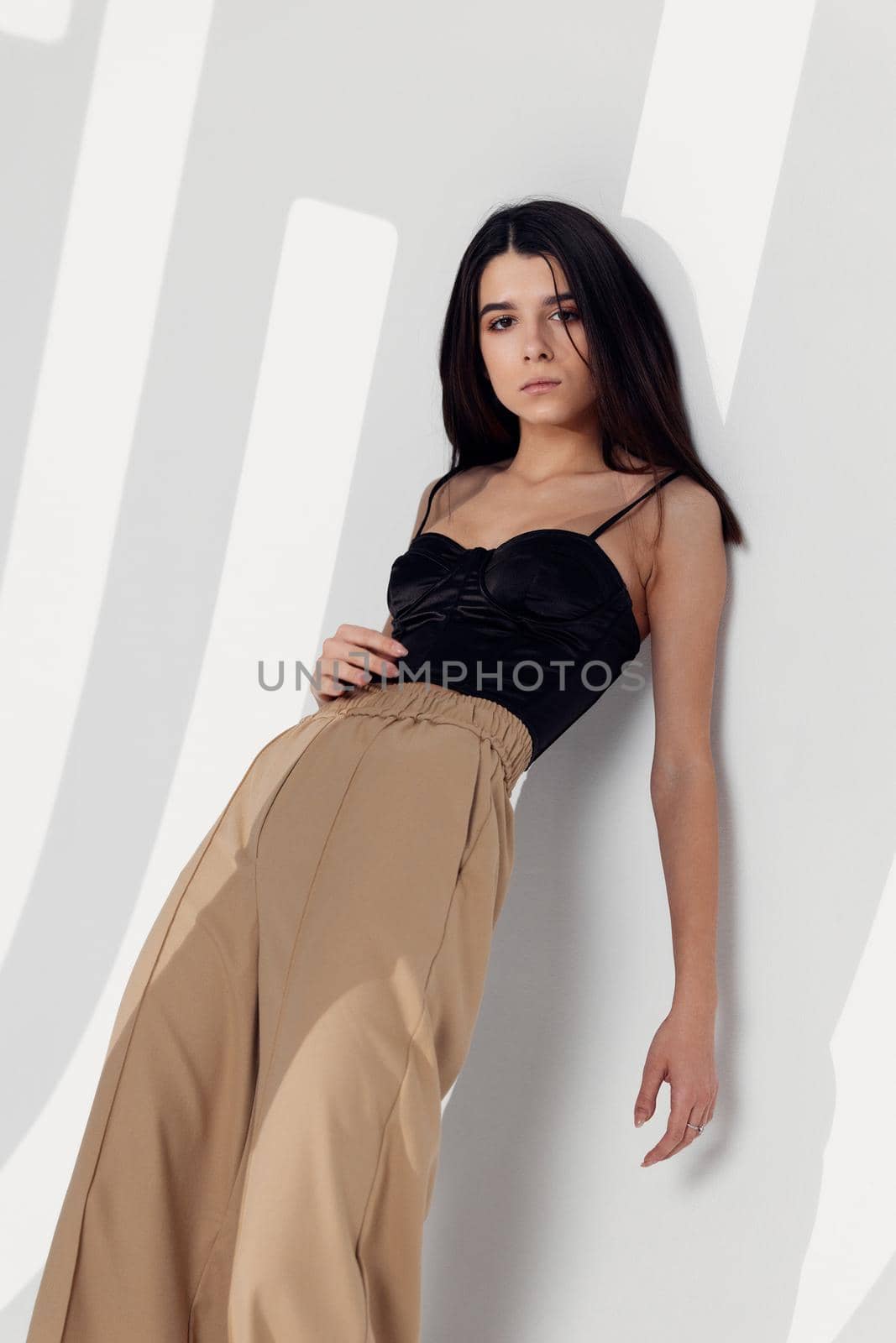 pretty brunette in a black top and beige trousers leaned against the wall in the room. High quality photo